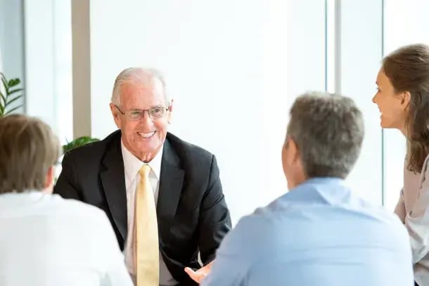 Un expert senior souriant échange avec trois interlocuteurs autour d'une table